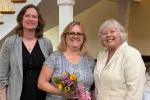 Three women smile at presentation of flowers to award recipient