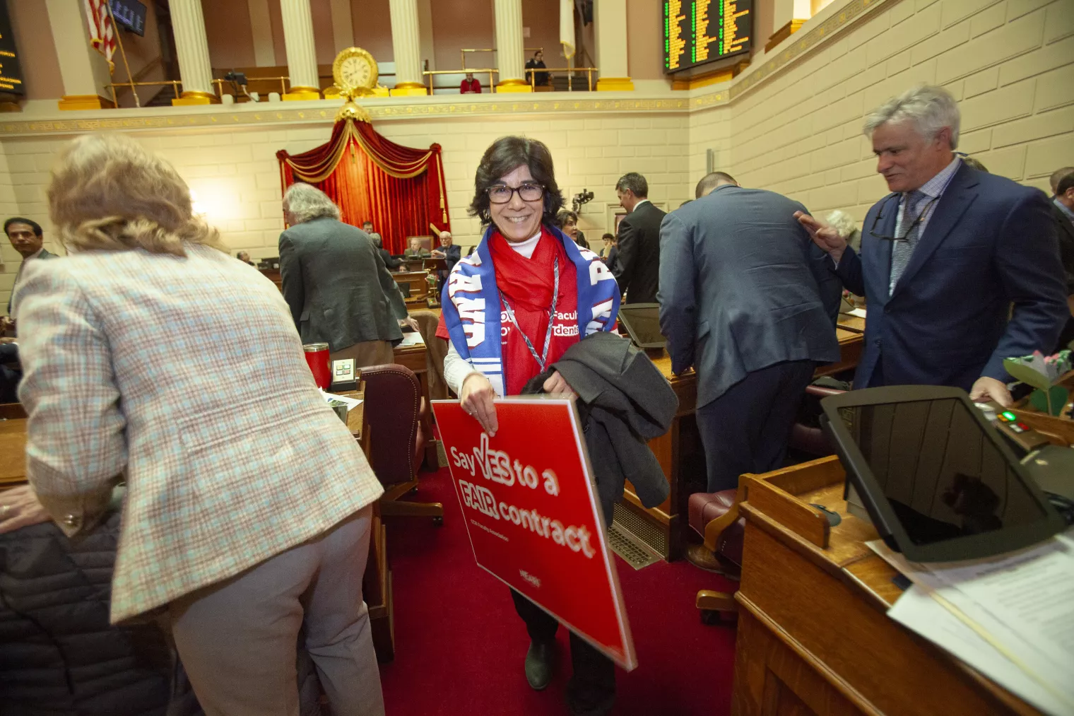 NEARI CCRI member on the floor in the Capitol holding "Say Yes to a Fair contract." sign at Lobby Day 2024