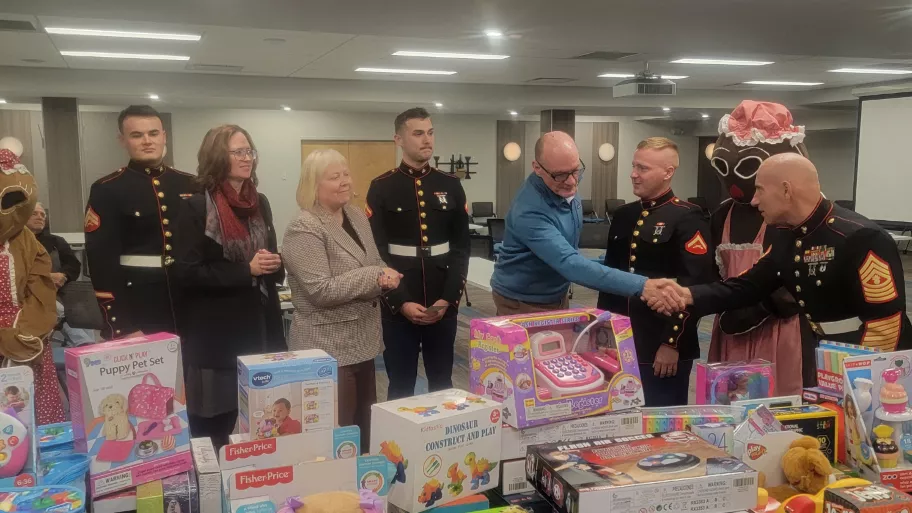 Group of people standing among a table piled with toys during a toy drive