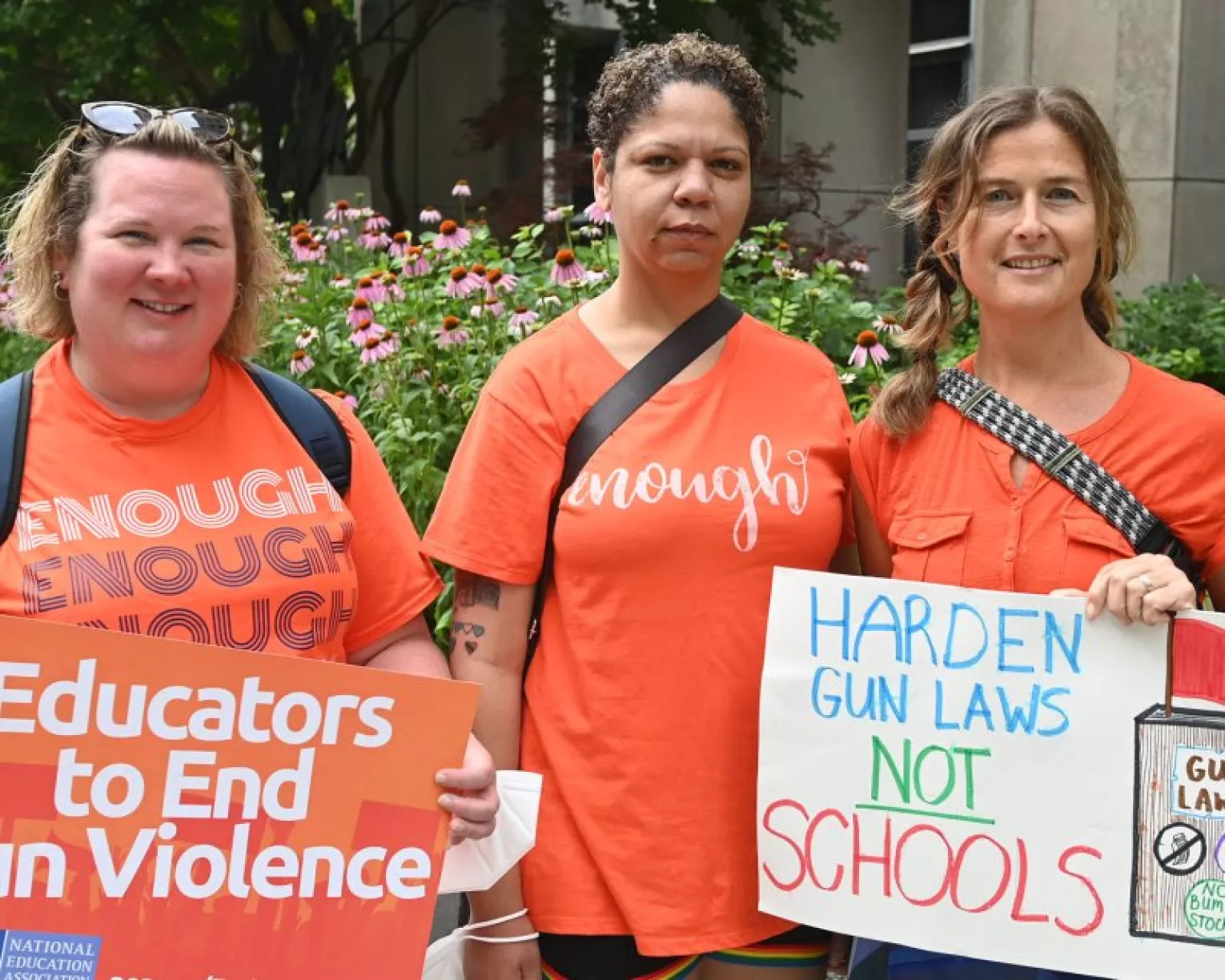 Three educators stand outside of the NEA building in Washington, D.C. wearing orange with signs that say "Educators to end gun violence" and "Harden gun laws, NOT schools." Their orange shirts also say "enough."