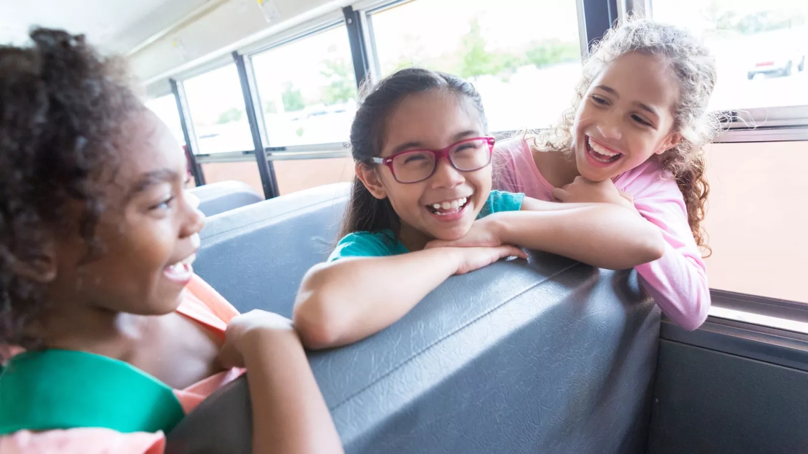 Three elementary school students laugh together on a school bus.