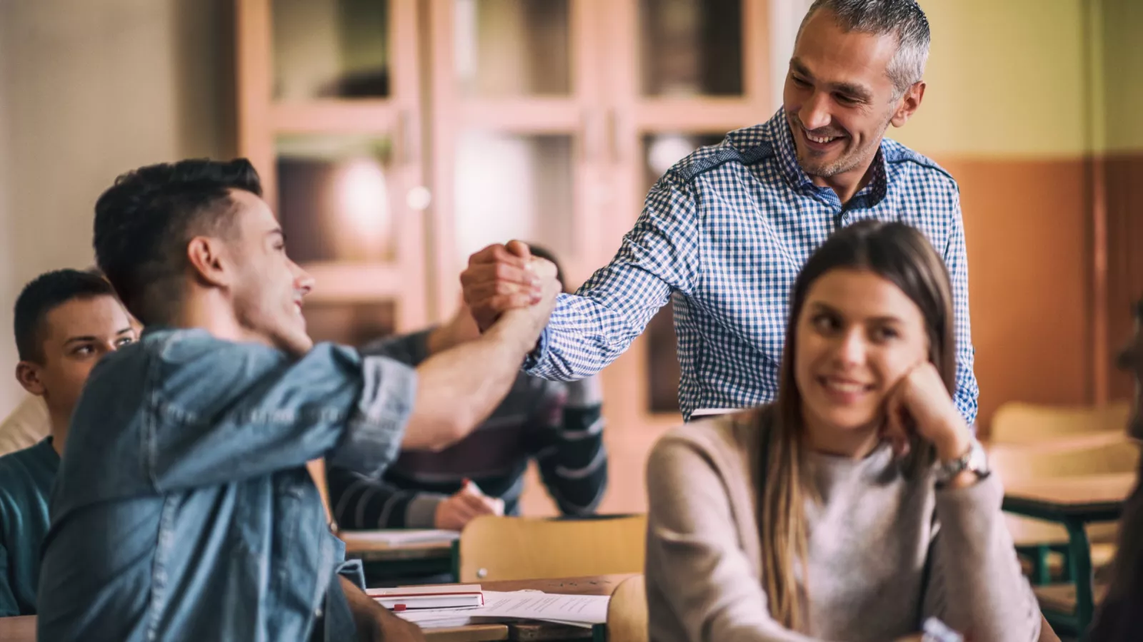 A high school teacher fist bumps a student. Both are smiling.