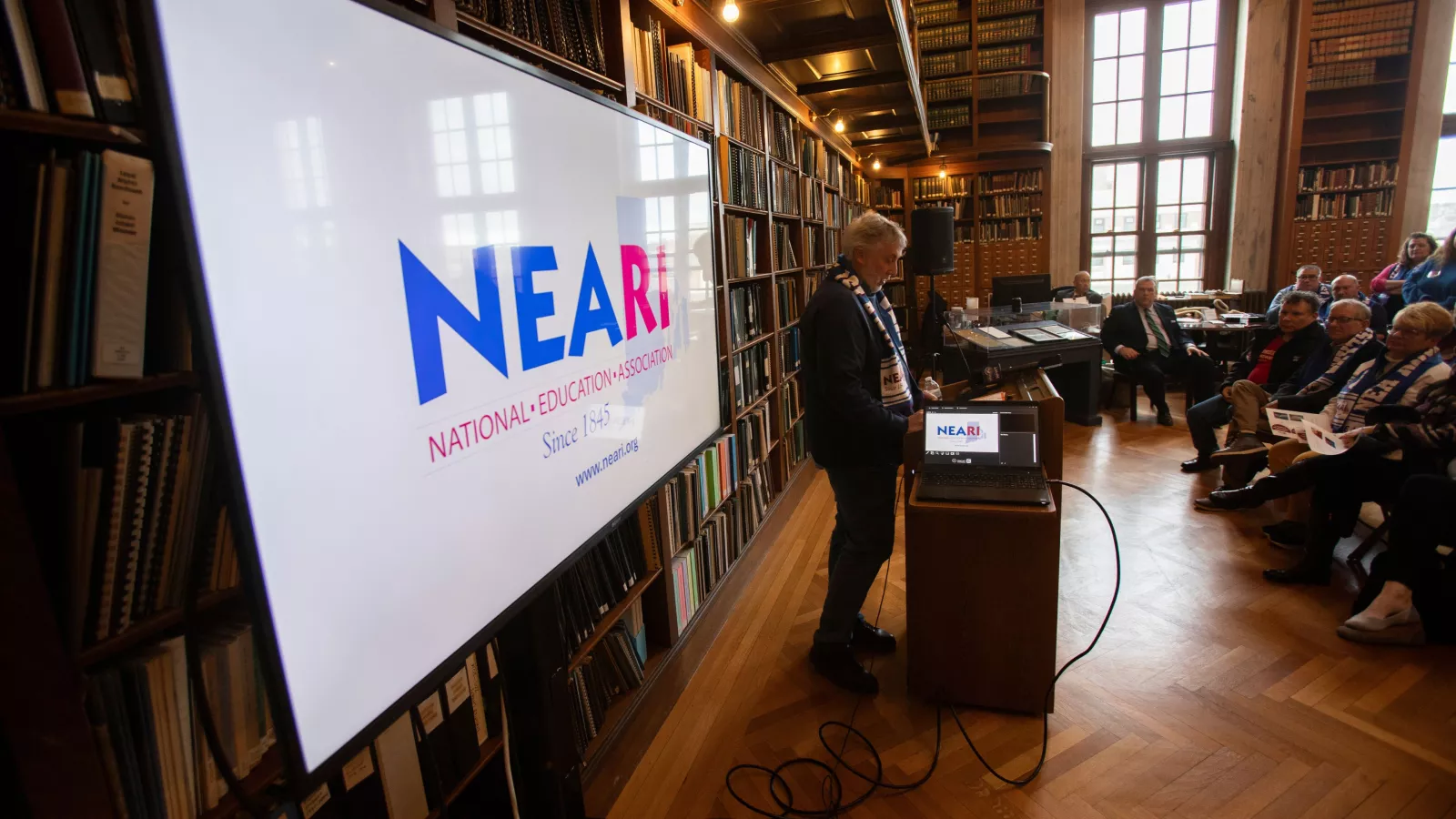 A NEARI member stands at the podium with a mic in the legislative agenda briefing during the 2024 Lobby Day at the Statehouse.