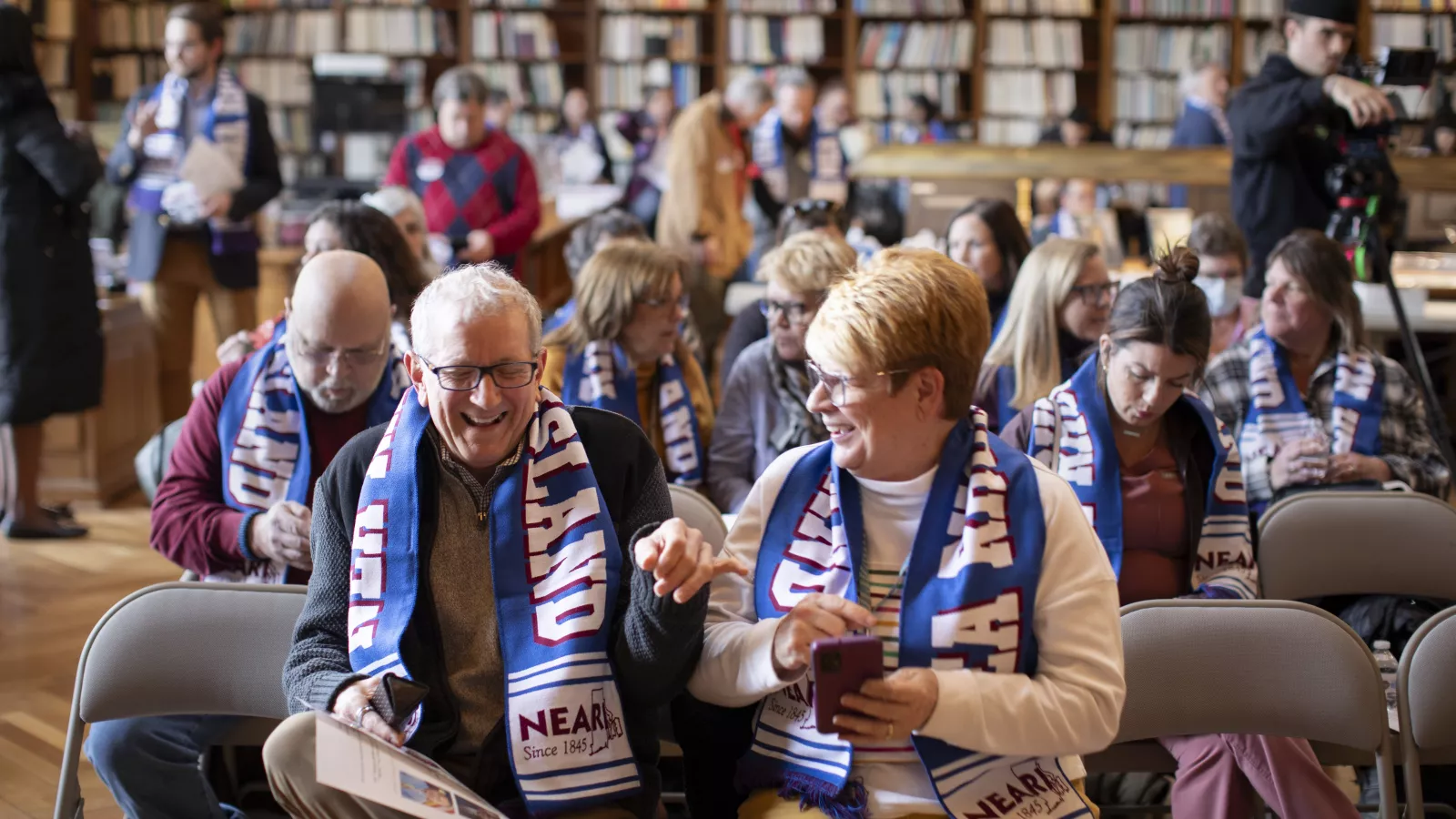 NEARI members wearing NEARI branded scarves laugh together in folding chairs at lobby day in 2024.