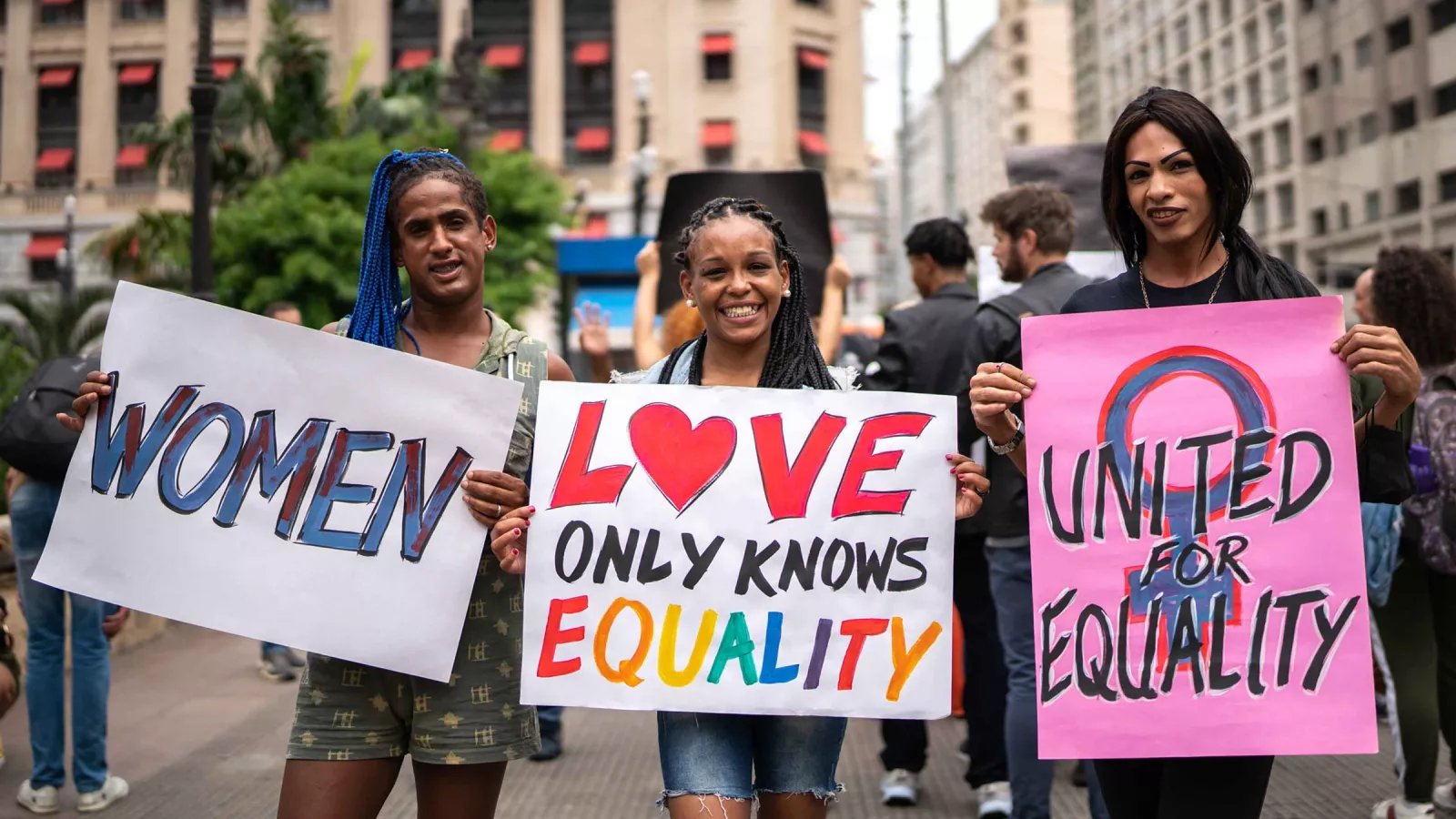 Transwomen marching and holding signs that say "women," "love only knows equality," and "united for equality"