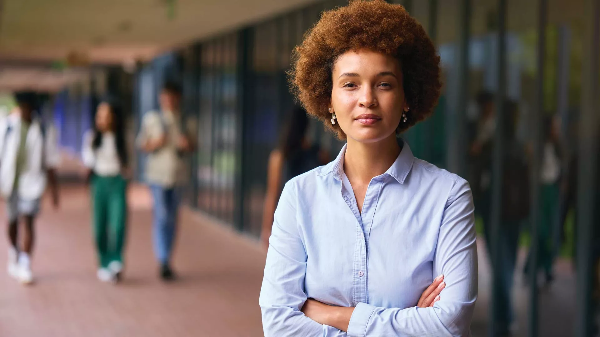 Black female teacher standing in outside corridor with students in the background.