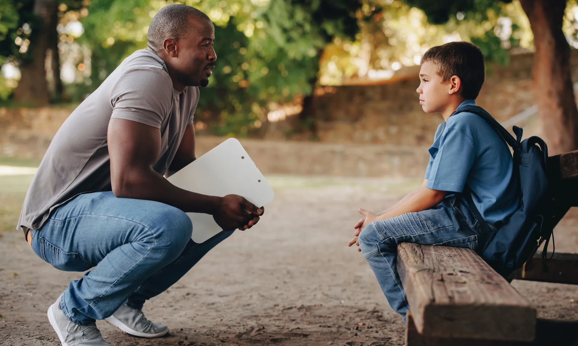male counselor stoops down to talk to an upset child on a bench outdoors