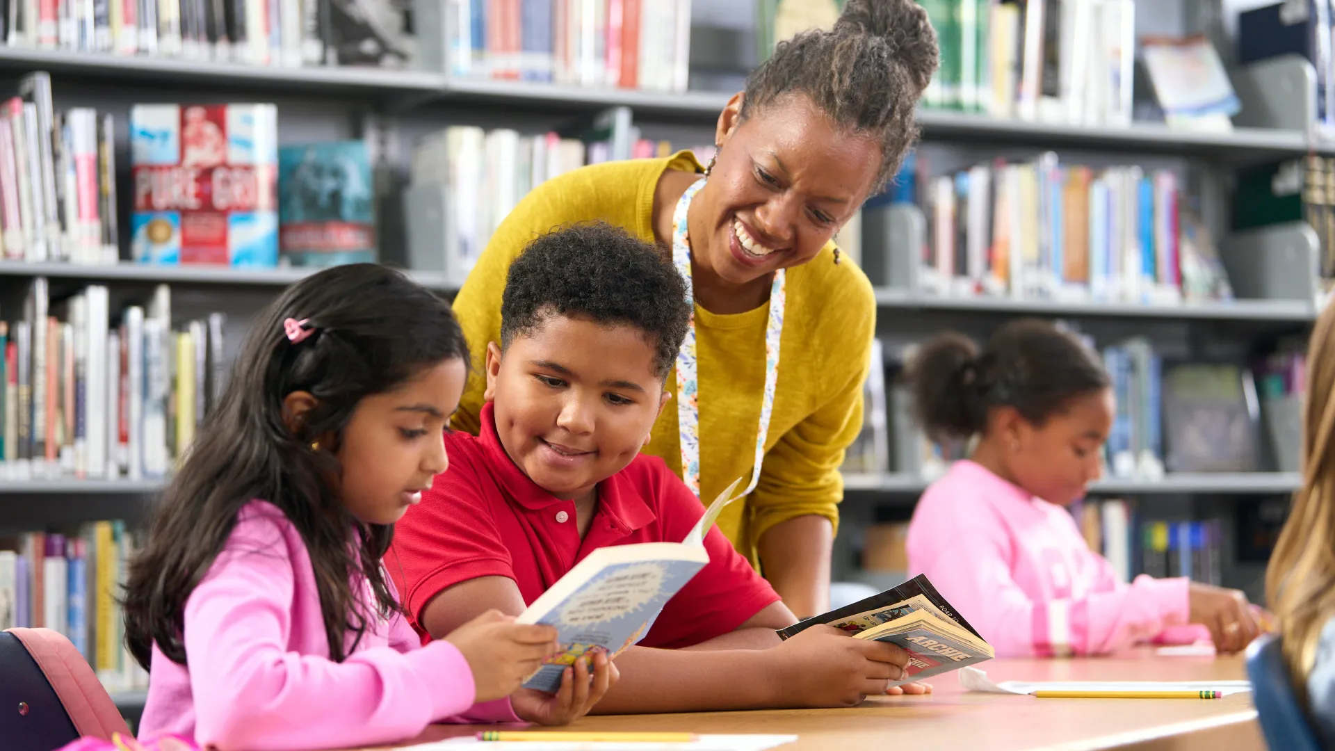 Librarian leans over seated students at the library who are reading a book