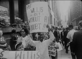 A black and white historic image of a person protesting  and holidng a sign that reads "Put Willis Out, Without a Doubt."