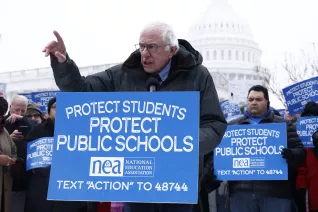 Bernie Sanders stands behind a sign with the U.S. Capitol as a backdrop.
