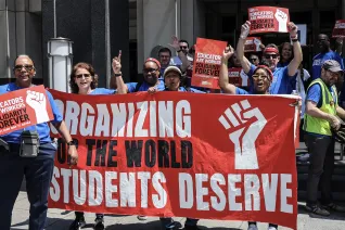 Educators in blue t-shirts stand outside behind a red banner that says Organizing for the world students deserve