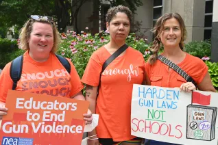 three educators wear orange and carry signs to protest gun violence