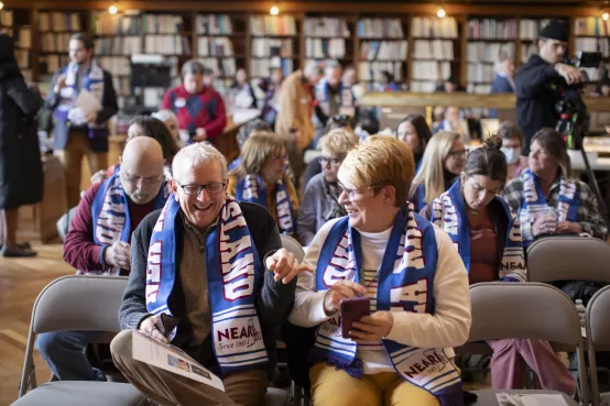 NEARI members wearing NEARI branded scarves laugh together in folding chairs at lobby day in 2024.