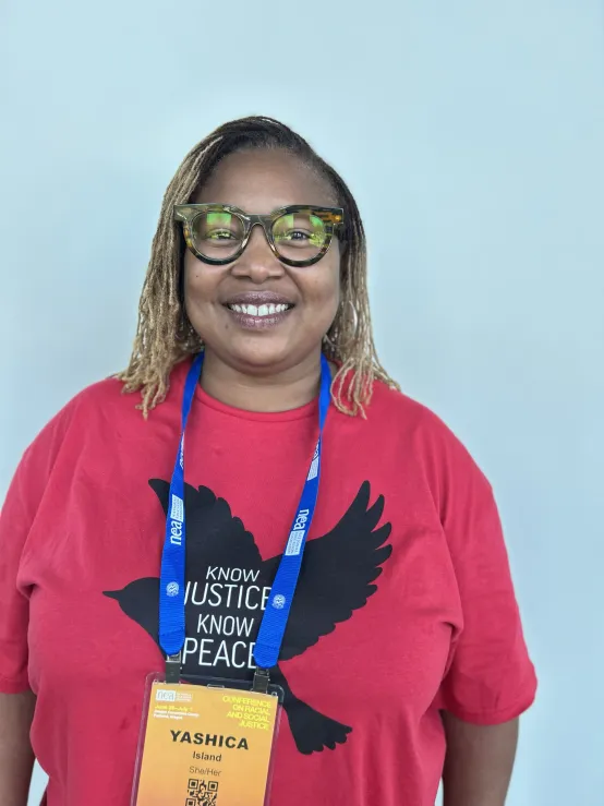 A woman in a red shirt featuring a bird design with the message "Know Justice Know Piece", smiling.