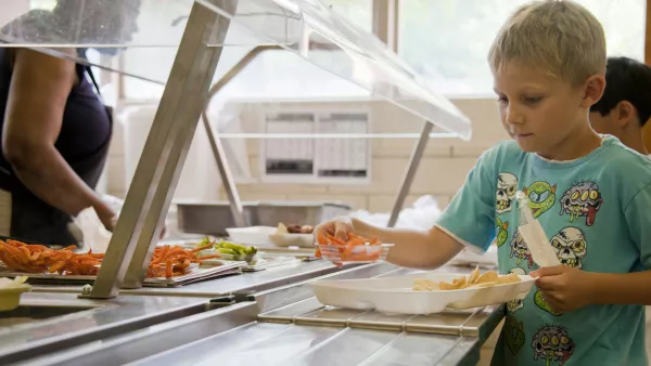 An elementary school student moves a lunch tray down the cafeteria line. On the line, you can see that the child has a wide variety of fresh vegetables to choose from.