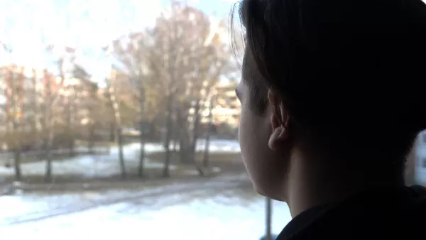 A student's profile can be seen, with face or features not visible, looking out a window at a snowy lawn.