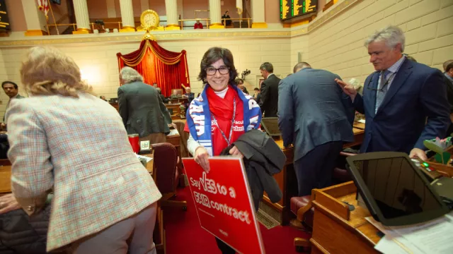 NEARI CCRI member on the floor in the Capitol holding "Say Yes to a Fair contract." sign on Lobby Day 2024
