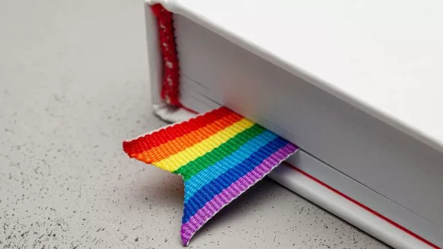 A pride flag ribbon bookmark peeks out a closed book.