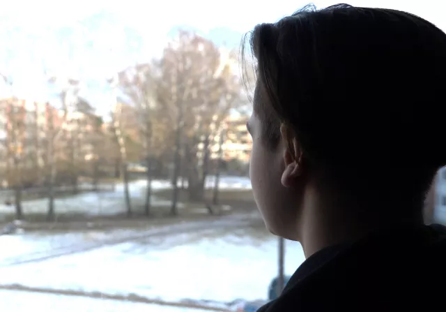 A student's profile can be seen, with face or features not visible, looking out a window at a snowy lawn.