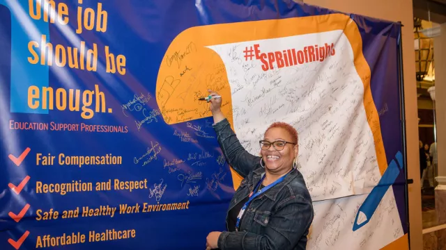An ESP member stands next to a big banner of the ESP bill of right as she signs and smiles for a picture.