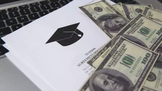 Several one-hundred dollar bills are lying on top of a paper reading "tuition agreement," which is on top of a black keyboard.