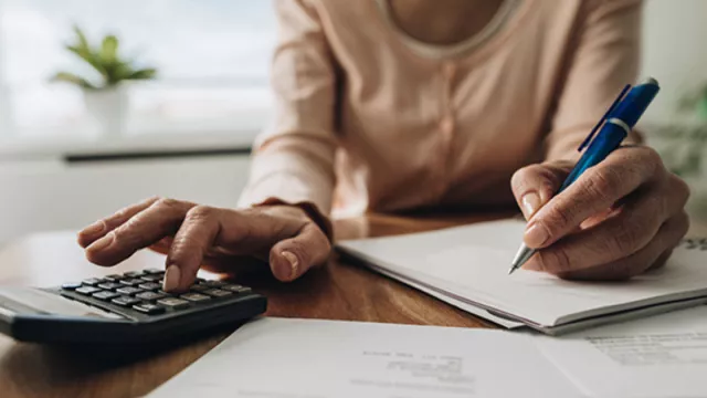 A woman going over finances with a calculator, pen, and paper.