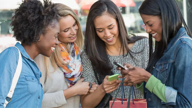 A group of young women crowd around a few phones, smiling.