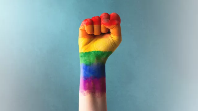 a person's fist painted with rainbow colors of the Pride flag