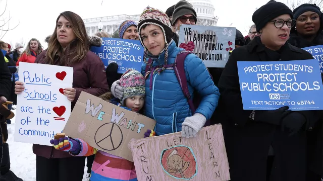 protesters hold signs in support of public schools outside the nation's Capitol in February 2025