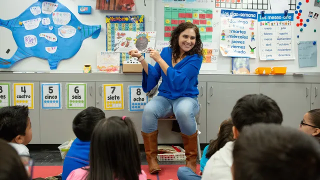 Teacher holds up book in front a class of students.