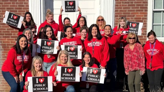 Teachers wearing red at Rockwell Elementary in Bristol hold I lOve Public Schools signs