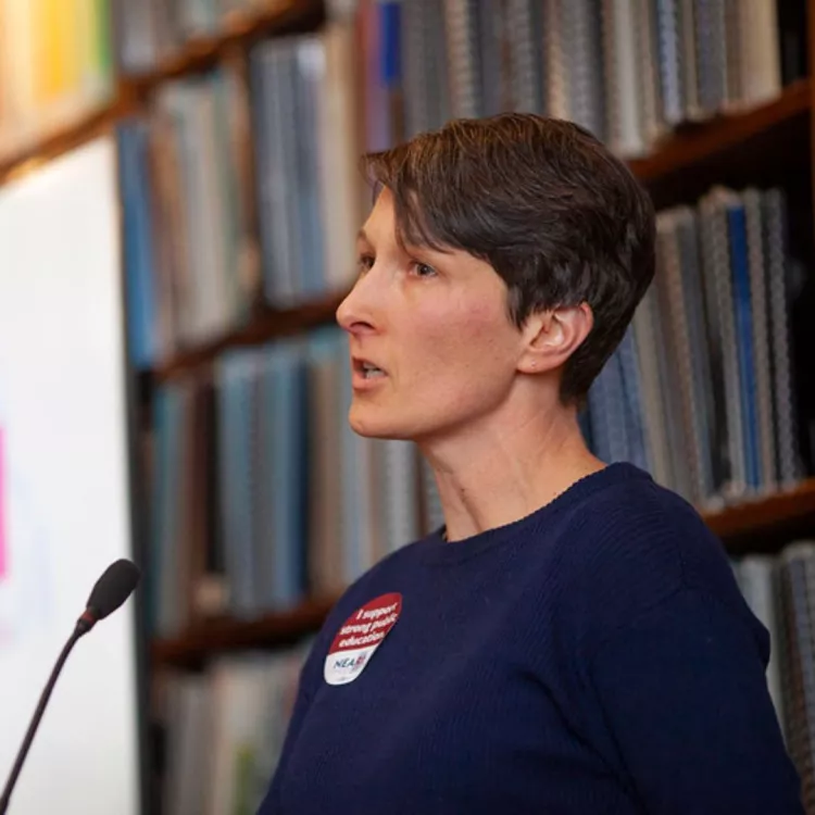 Jen Saarinen, a math teacher, speaks about gun violence into a microphone at a podium during NEARI's 2024 Lobby Day.