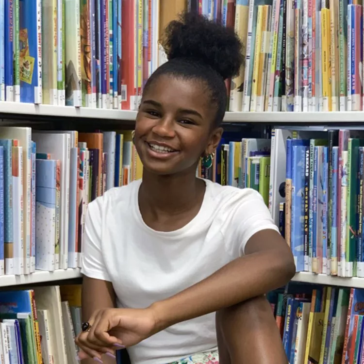 Marley Dias sits between two bookshelves with a big smile on her face.